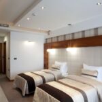 Δίκλινο δωμάτιο με δύο κρεβάτια, μοντέρνα διακόσμηση, φωτιστικά οροφής και ξύλινη λεπτομέρεια στο κεφαλάρι.