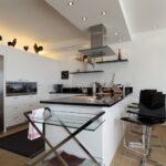 Σύγχρονη κουζίνα με λευκά ντουλάπια, μαύρους πάγκους και μεταλλικές καρέκλες μπαρ για μοντέρνο στυλ.