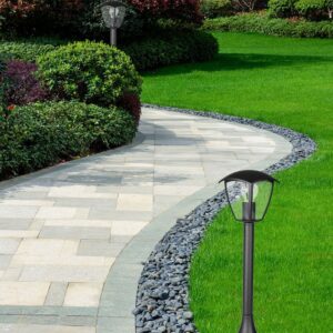Πλακόστρωτο μονοπάτι με φωτισμό κήπου, περιτριγυρισμένο από πράσινο γρασίδι και θάμνους.