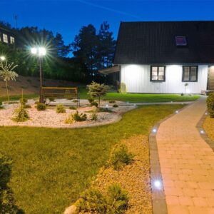 Εξωτερικός χώρος με φωτισμό κήπου και πλακόστρωτο μονοπάτι δίπλα σε εξοχικό σπίτι τη νύχτα.