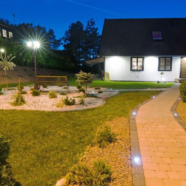 Εξωτερικός χώρος με φωτισμό κήπου και πλακόστρωτο μονοπάτι δίπλα σε εξοχικό σπίτι τη νύχτα.
