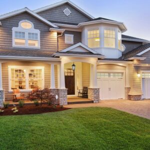 Διώροφο σπίτι παραδοσιακής αρχιτεκτονικής με φωτισμένες βεράντες και γκαράζ, καταξιωμένο στον κήπο.