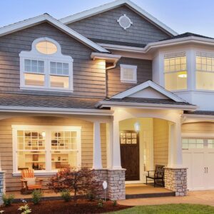 Σπίτι διώροφο με γκρι και λευκή όψη, κήπος μπροστά και ζεστός εξωτερικός φωτισμός.