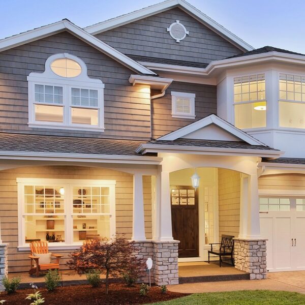 Σπίτι διώροφο με γκρι και λευκή όψη, κήπος μπροστά και ζεστός εξωτερικός φωτισμός.