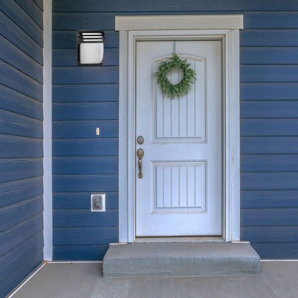 Φωτιστικό εξωτερικού χώρου σε φωτεινό λευκό και μαύρο, τοποθετημένο δίπλα σε λευκή εξώπορτα με γαλάζιο φόντο.